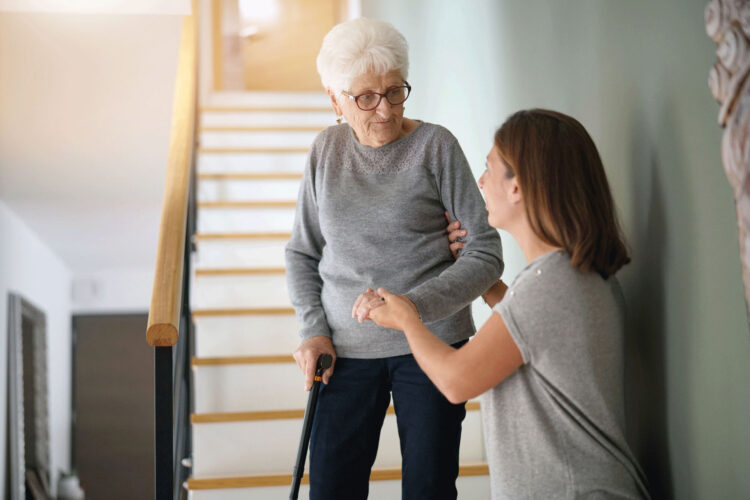Female carer supporting an older lady walking down stairs