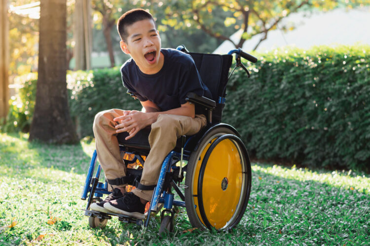 Smiling teenage boy in a wheelchair in a sunny garden